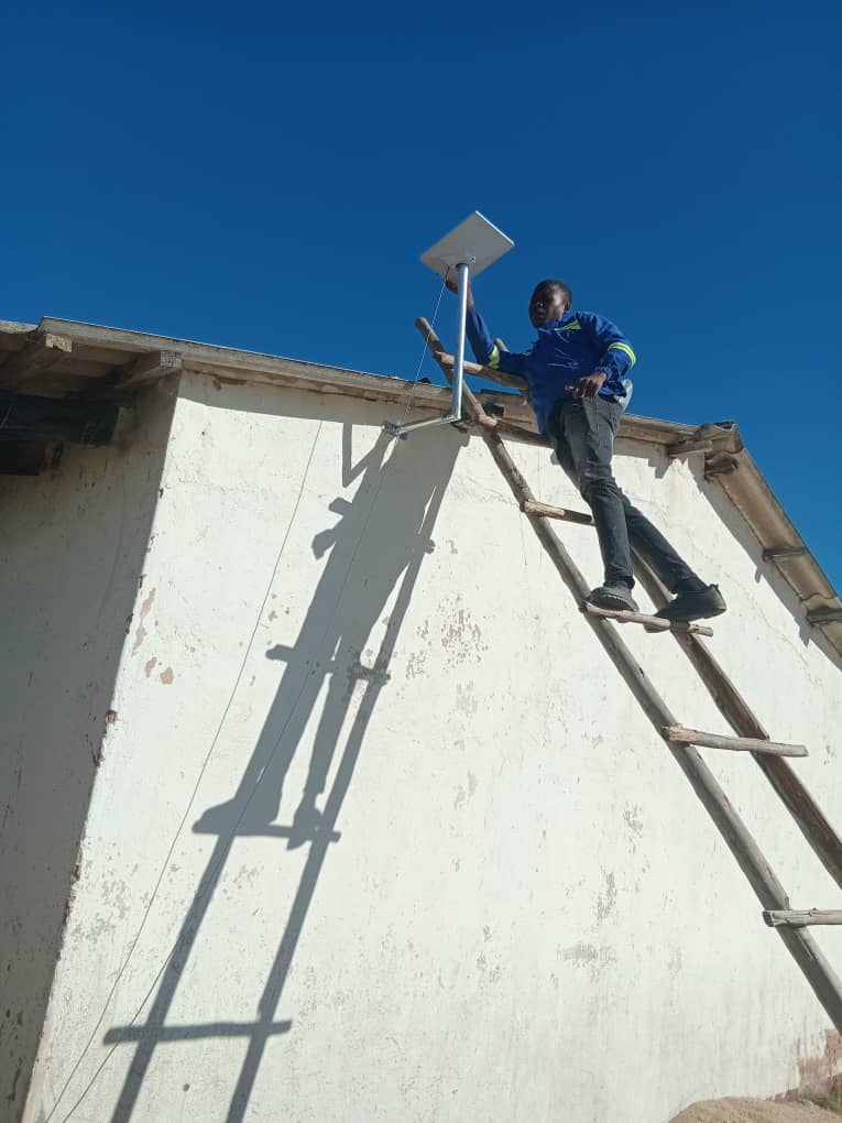 Technician mounting Starlink dish from ladder